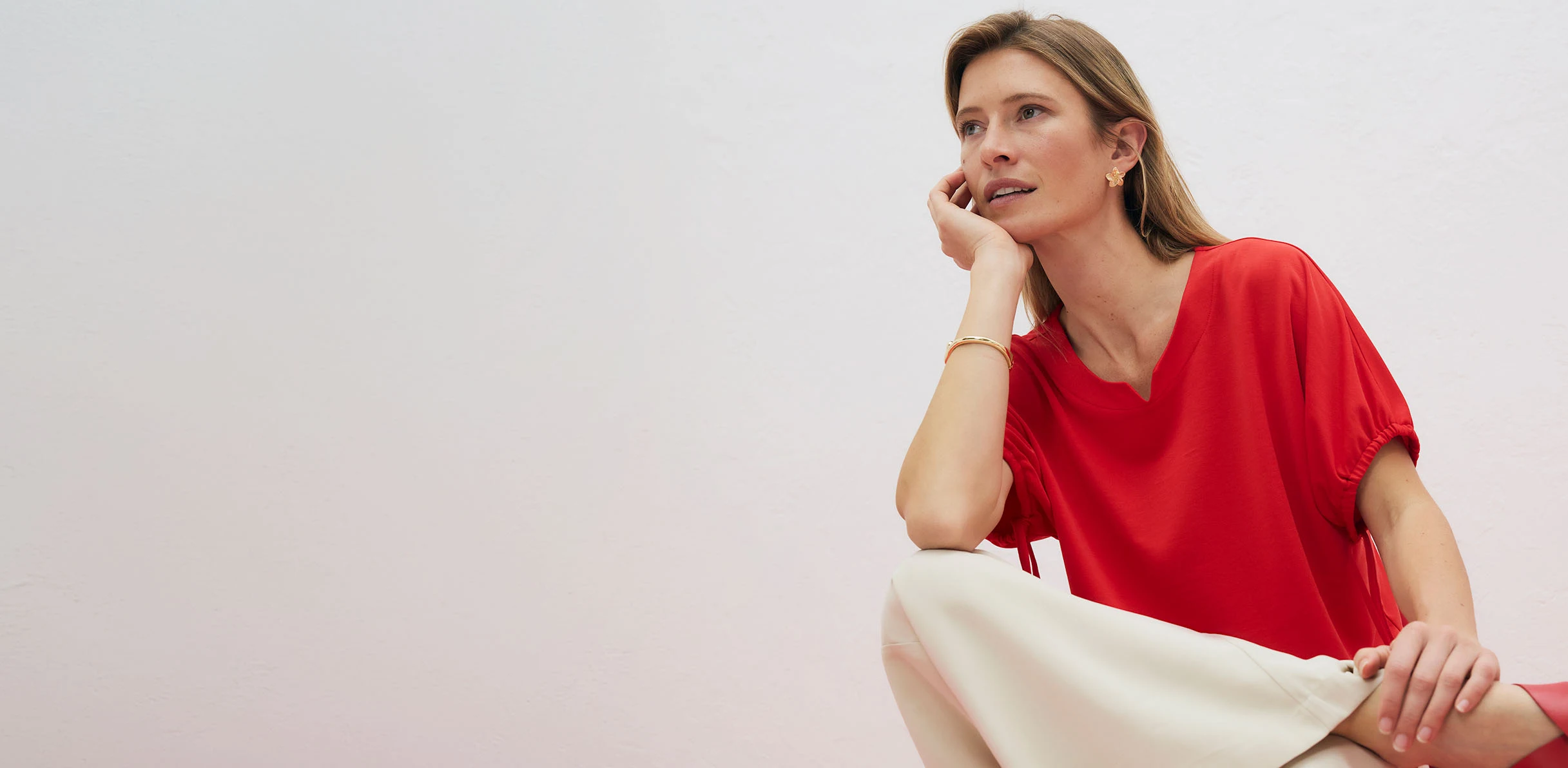 Elegáns, piros póló V-nyakkivágással, világos nadrággal kombinálva.